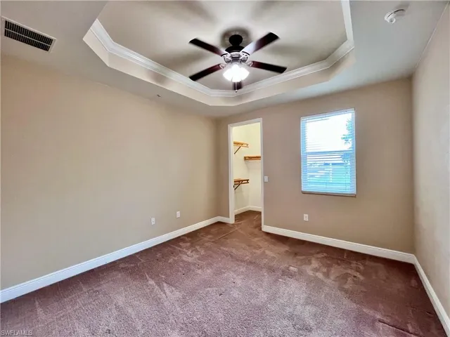 Bedroom #2 with walk in closet, natural light, hurricane windows and shutters, featuring ornamental molding, carpet flooring, a raised ceiling and ceiling fan