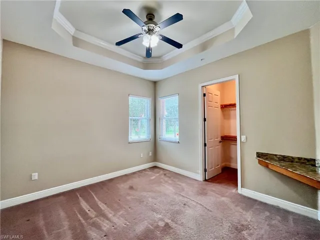 Bedroom #3 with a walk in closet, crown molding, a tray ceiling, carpet floors, and a ceiling fan
