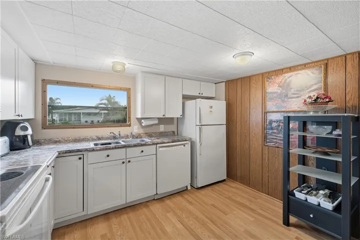 Kitchen with white cabinetry, white appliances, wooden walls, and light wood-style floors