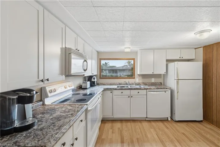 Kitchen with white appliances, white cabinets, dark countertops, and light wood-type flooring