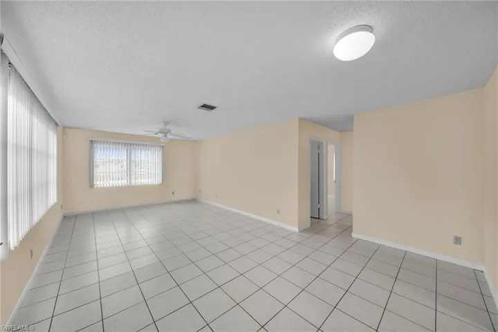 Empty room with a textured ceiling, light tile patterned floors, and ceiling fan