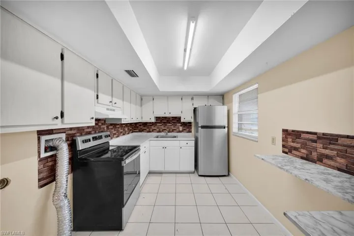 Kitchen with stainless steel appliances, backsplash, light tile patterned floors, and white cabinetry