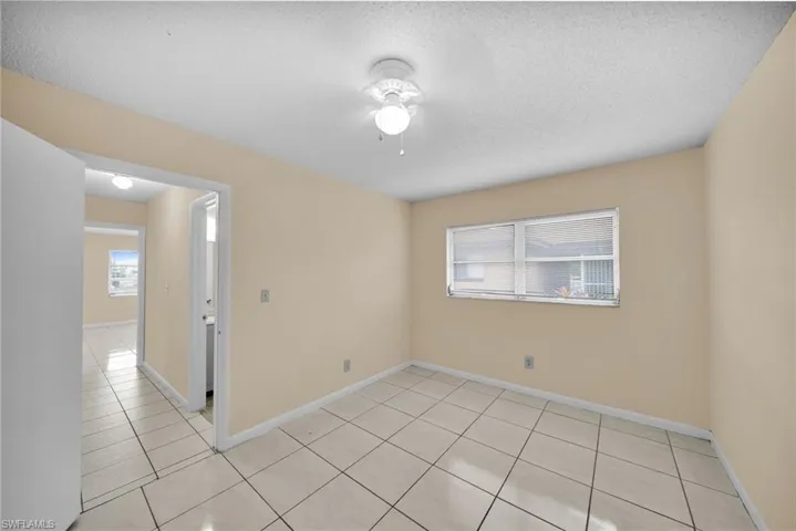 Empty room with a textured ceiling, light tile patterned floors, plenty of natural light, and ceiling fan