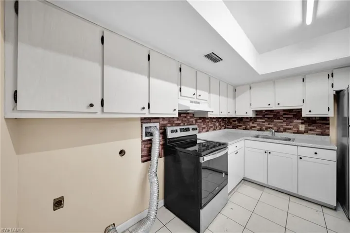 Kitchen with electric stove, light countertops, tasteful backsplash, freestanding refrigerator, and white cabinetry