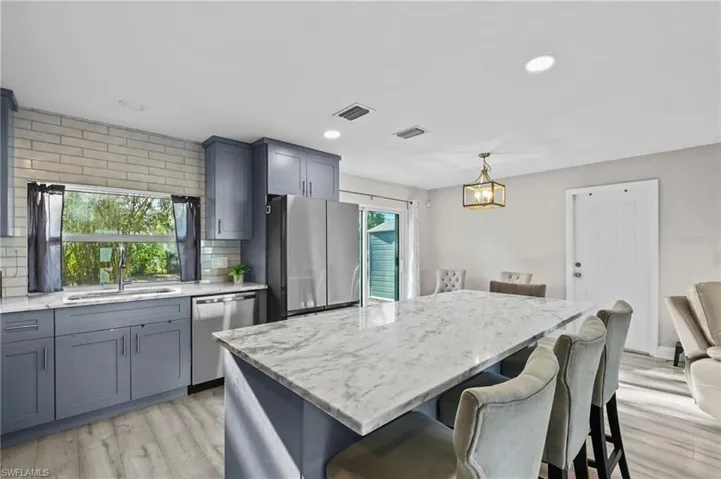 Kitchen featuring tasteful backsplash, appliances with stainless steel finishes, a kitchen bar, light stone counters, and recessed lighting