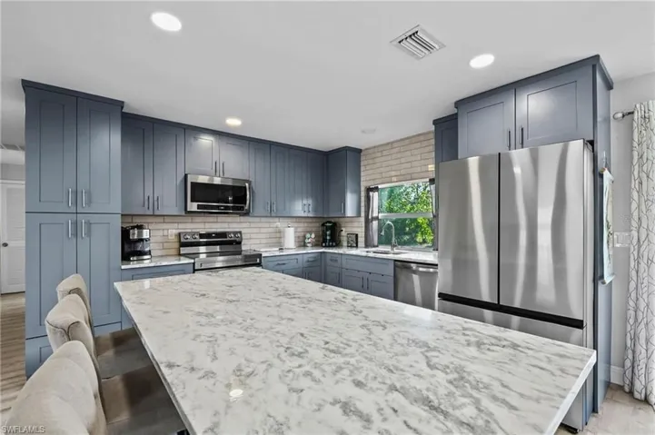 Kitchen with appliances with stainless steel finishes, a kitchen bar, a kitchen island, backsplash, and light stone counters