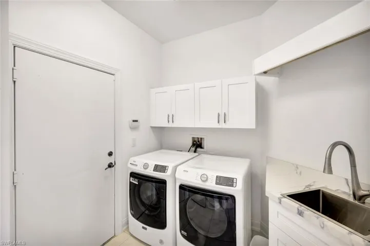 Well equipped laundry room with utility sink, overhead cabinetry and high efficiency washer/dryer
