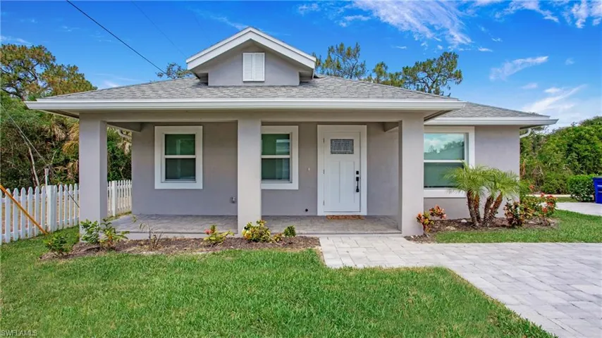 Contemporary single-story residence featuring a covered front porch, white picket fence, and paver stone driveway