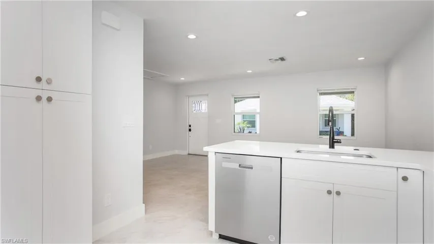 Modern kitchen island with a built-in stainless steel dishwasher, undermount sink, matte black faucet, and white countertop