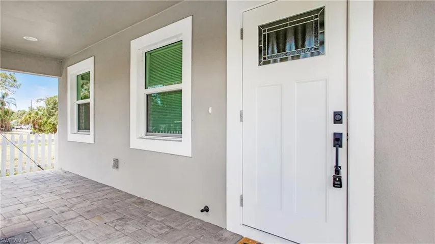 Covered entryway featuring a white paneled door with decorative glass inlay, black hardware, and two windows with white trim
