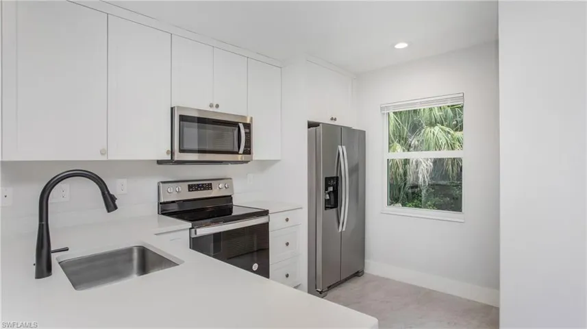 Modern kitchen featuring white cabinetry with silver hardware, stainless steel appliances, a matte black faucet, and light-toned countertops
