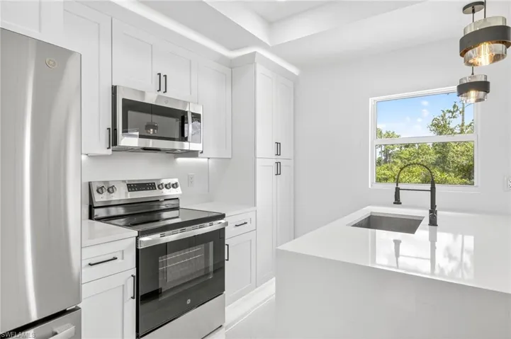 Kitchen featuring stainless steel appliances, white cabinetry, decorative light fixtures, and light stone counters