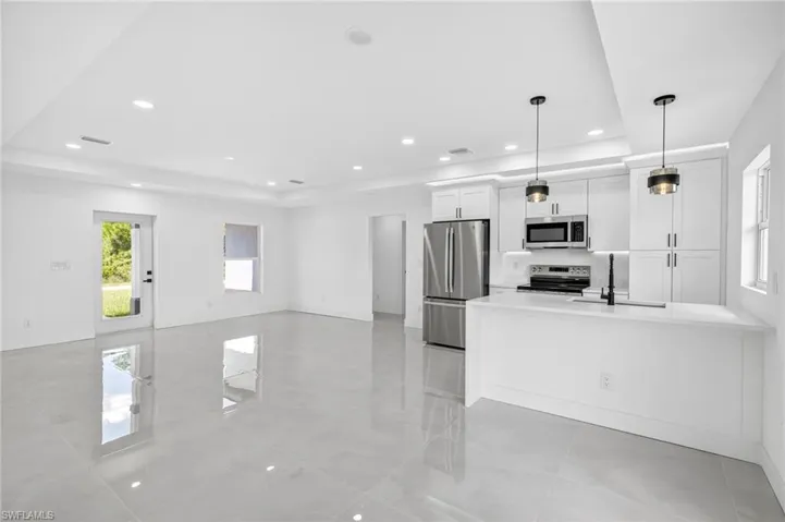 Kitchen featuring appliances with stainless steel finishes, open floor plan, white cabinets, decorative light fixtures, and a peninsula