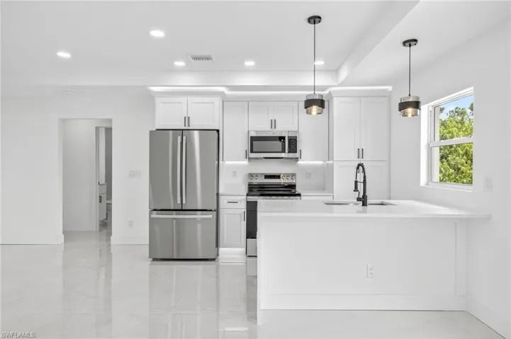 Kitchen with white cabinets, appliances with stainless steel finishes, recessed lighting, a peninsula, and light stone countertops