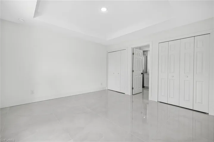 Unfurnished bedroom featuring a tray ceiling, two closets, light tile patterned floors, and recessed lighting