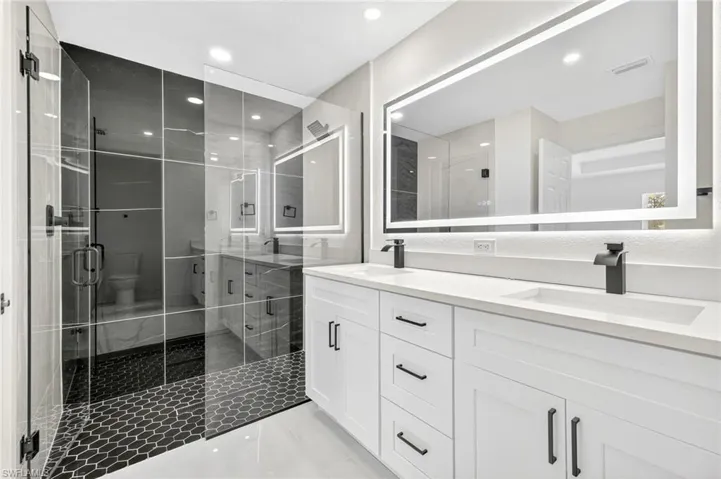 Bathroom featuring double vanity, a stall shower, light tile patterned flooring, and recessed lighting