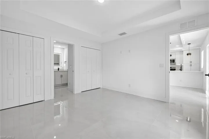 Unfurnished bedroom featuring multiple closets, a tray ceiling, recessed lighting, connected bathroom, and light tile patterned floors