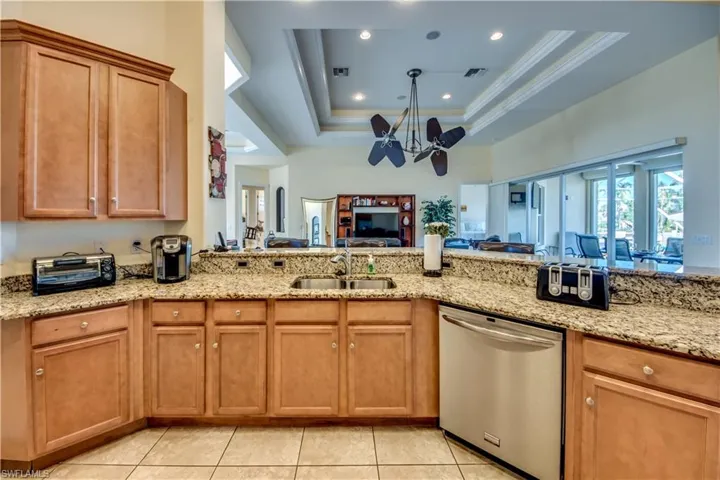Kitchen featuring dishwasher, sink, a tray ceiling, light tile patterned flooring, and light stone counters
