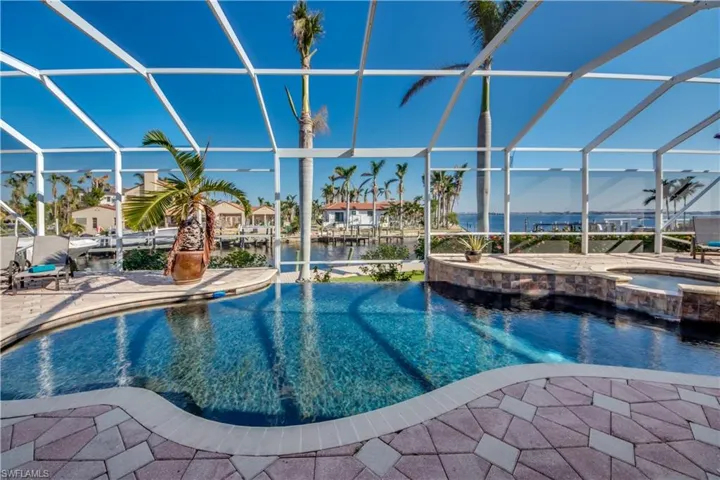 View of pool featuring glass enclosure, a patio area, a water view, and an in ground hot tub