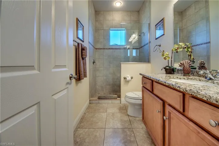 Bathroom featuring tile patterned floors, vanity, toilet, and tiled shower