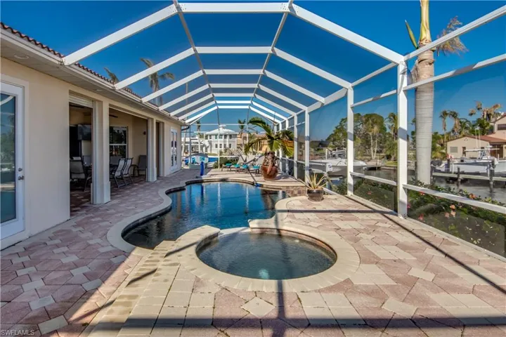 View of swimming pool featuring a patio area, an in ground hot tub, a water view, and glass enclosure