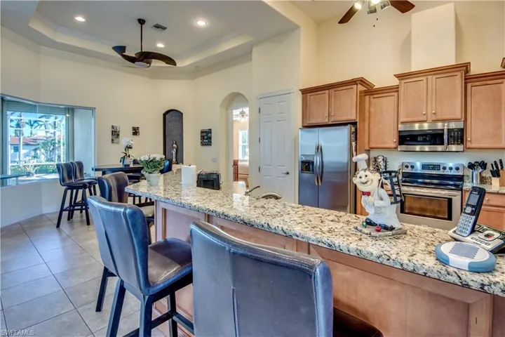 Kitchen featuring light stone countertops, a raised ceiling, a kitchen breakfast bar, a towering ceiling, and appliances with stainless steel finishes