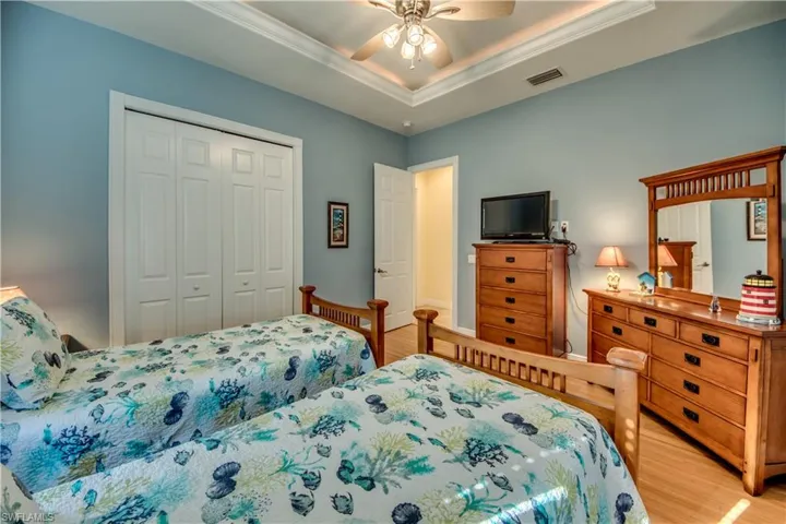 Bedroom with ceiling fan, a raised ceiling, light hardwood / wood-style flooring, crown molding, and a closet