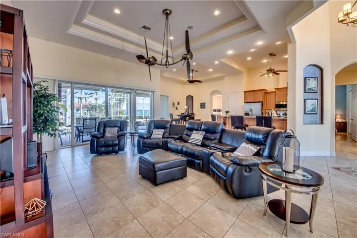 Tiled living room featuring ceiling fan with notable chandelier, a towering ceiling, and a tray ceiling