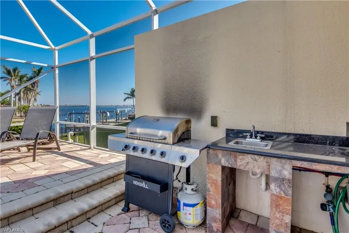 View of patio / terrace featuring a lanai, grilling area, sink, and a water view