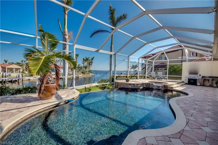 View of swimming pool with a patio area, an in ground hot tub, a water view, and glass enclosure