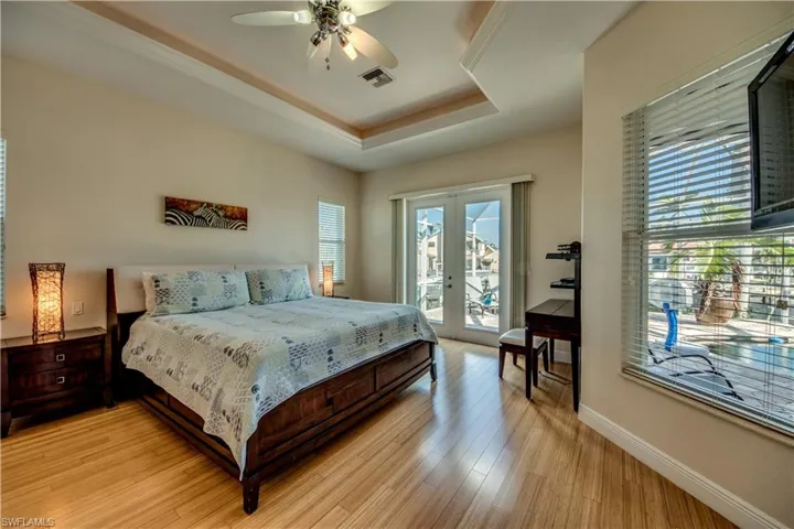 Bedroom featuring french doors, light wood-type flooring, access to outside, a tray ceiling, and ceiling fan