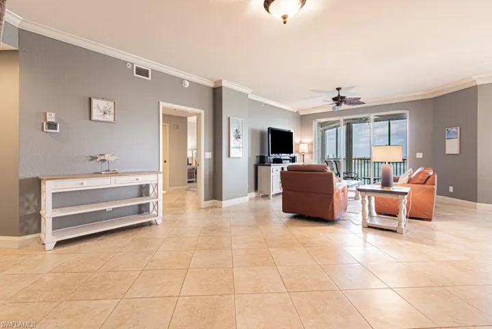 Living room featuring ornamental molding, ceiling fan, a textured wall, and light tile patterned floors