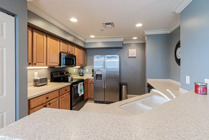 Kitchen with stainless steel appliances, ornamental molding, recessed lighting, and light stone countertops
