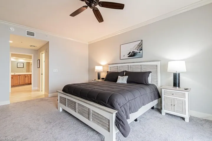 Bedroom with ornamental molding, light colored carpet, a ceiling fan, and connected bathroom