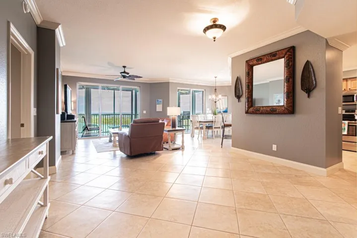 Living area with ceiling fan, crown molding, a textured wall, light tile patterned floors, and a chandelier