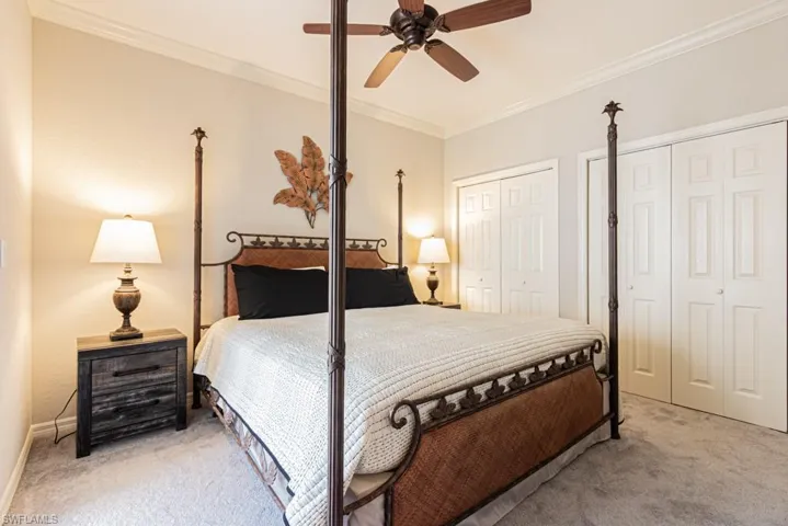 Carpeted bedroom with multiple closets, ornamental molding, and ceiling fan