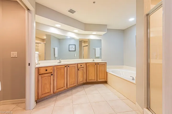 Bathroom featuring a bath, double vanity, light tile patterned floors, a shower stall, and recessed lighting