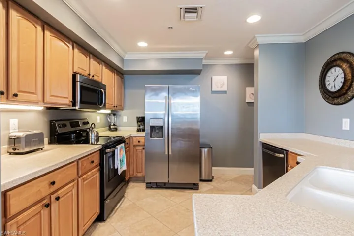 Kitchen featuring appliances with stainless steel finishes, light tile patterned floors, crown molding, recessed lighting, and light stone countertops