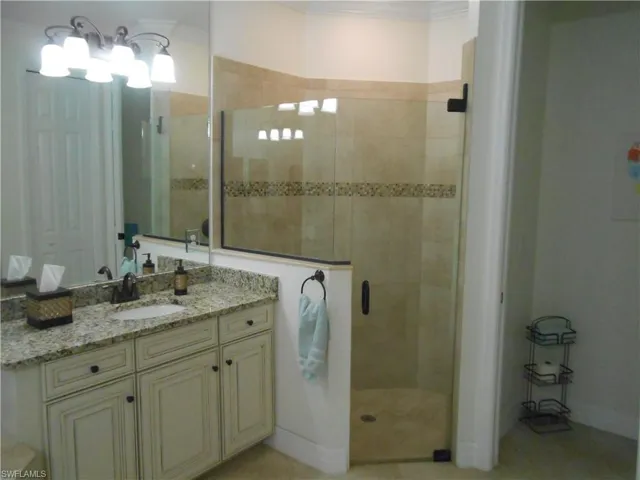 Bathroom featuring a stall shower, vanity, ornamental molding, and light tile patterned floors