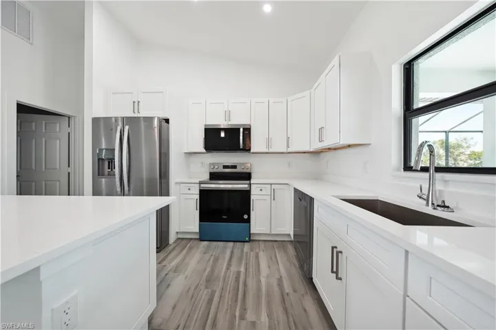 Modern kitchen with vaulted ceilings, white shaker-style cabinetry, and light wood-finish flooring