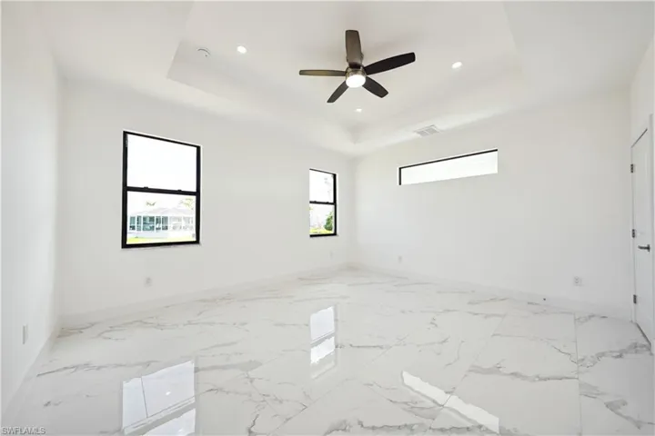 Spacious interior featuring large format tile flooring, a tray ceiling, recessed lighting, and a ceiling fan with integrated light fixture
