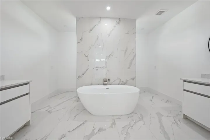 Freestanding soaking tub with a wall-mounted faucet, complemented by large format marbled-finish floor and wall tiles