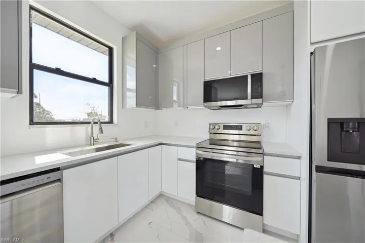 Modern kitchen featuring white flat-panel cabinetry, light-toned countertops, and stainless steel appliances including a range, microwave, dishwasher, and refrigerator