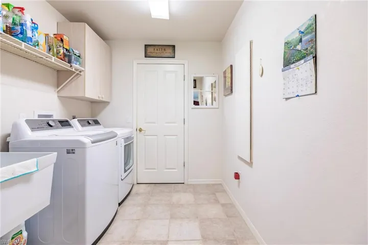 Clothes washing area featuring separate washer and dryer, sink, and light tile flooring