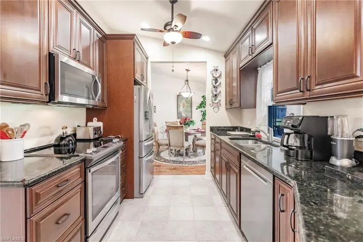 Kitchen with dark stone counters, ceiling fan, stainless steel appliances, light tile flooring, and sink