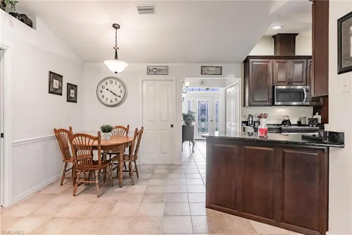 Kitchen with dark brown cabinetry, hanging light fixtures, range, and light tile flooring