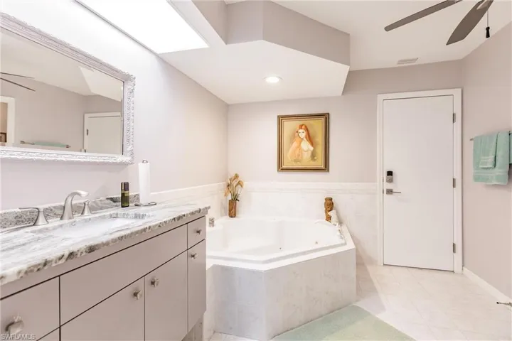 Bathroom featuring tile floors, tiled bath, large vanity, and ceiling fan