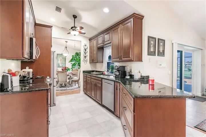 Kitchen featuring stainless steel appliances, dark stone countertops, ceiling fan, and light tile floors