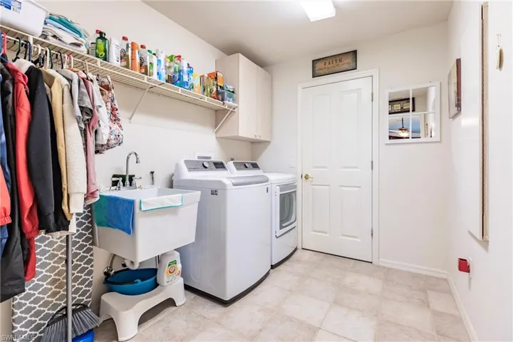 Washroom featuring sink, washing machine and clothes dryer, cabinets, and light tile floors