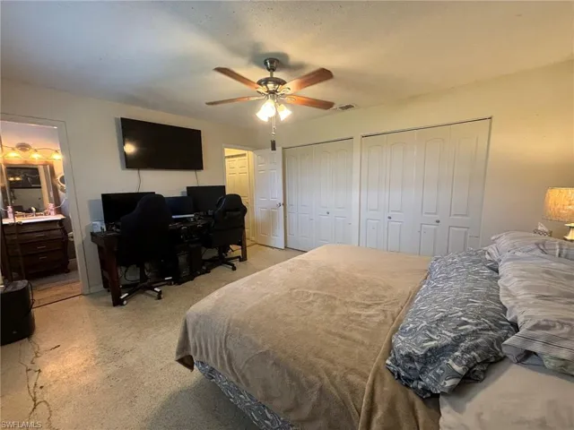 Bedroom featuring light carpet, multiple closets, and ceiling fan